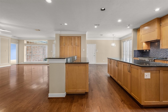 kitchen with a kitchen island, pendant lighting, backsplash, and dark stone counters