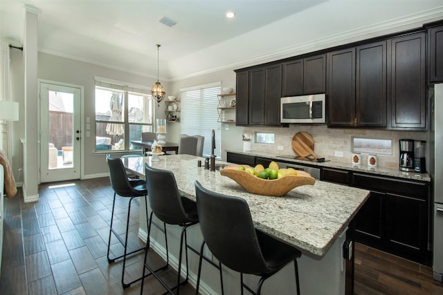 kitchen featuring sink, crown molding, hanging light fixtures, a center island with sink, and decorative backsplash