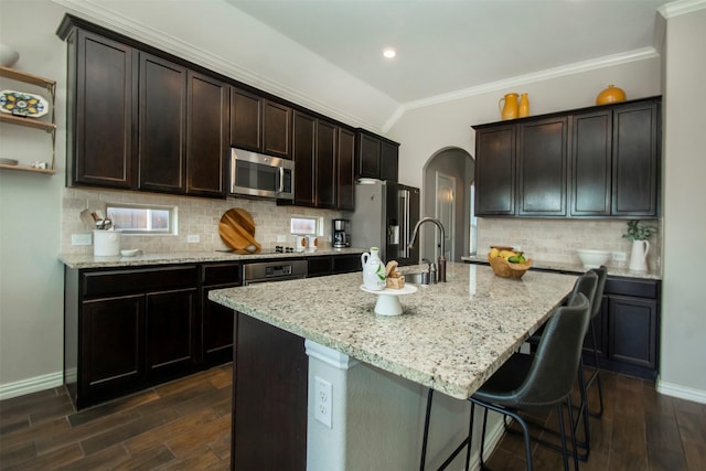 kitchen with dark hardwood / wood-style floors, dark brown cabinets, appliances with stainless steel finishes, and a center island with sink