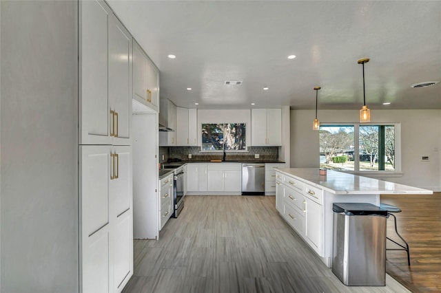 kitchen featuring white cabinetry, tasteful backsplash, decorative light fixtures, a center island, and appliances with stainless steel finishes