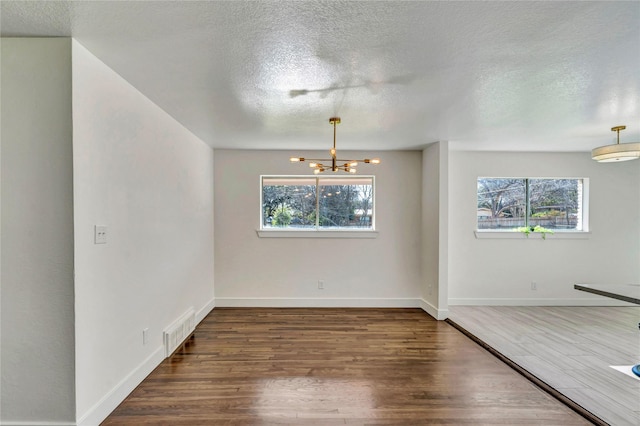 spare room with dark wood-type flooring, an inviting chandelier, a textured ceiling, and a wealth of natural light