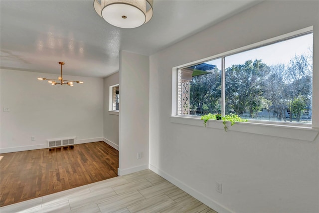 spare room featuring a notable chandelier and light wood-type flooring