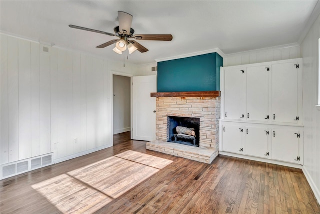 unfurnished living room with wood-type flooring, crown molding, ceiling fan, and a fireplace