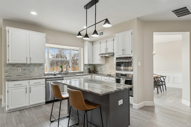 kitchen featuring visible vents, white cabinets, light stone countertops, stainless steel appliances, and a sink