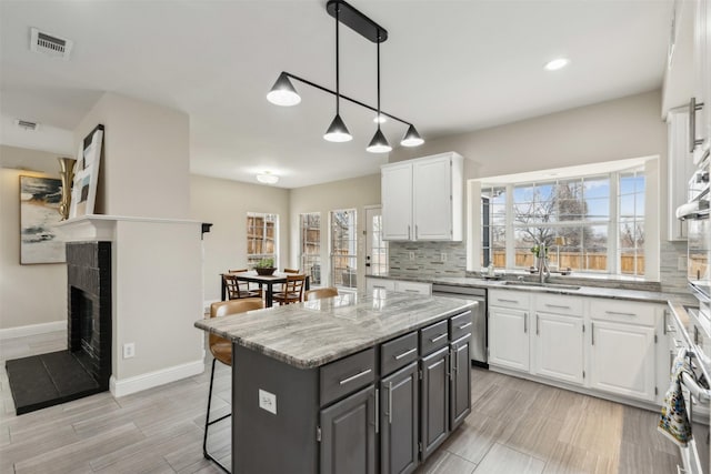 kitchen with sink, a center island, dishwasher, pendant lighting, and white cabinets