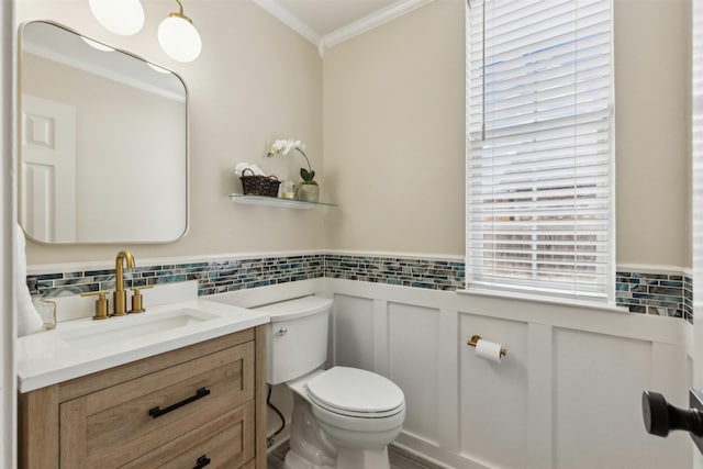 bathroom featuring a wainscoted wall, vanity, toilet, and crown molding