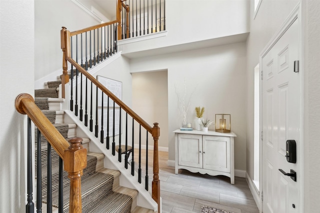 stairs with wood finish floors, a towering ceiling, and baseboards