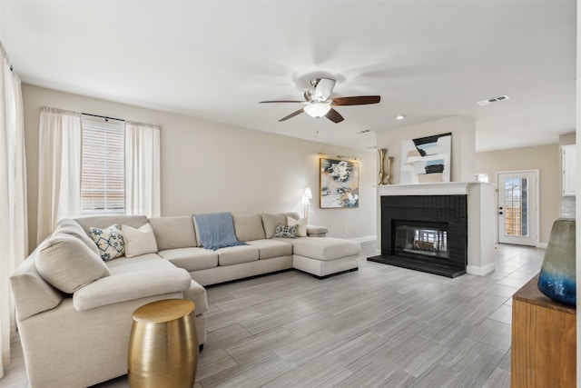 living area featuring visible vents, light wood-style floors, a brick fireplace, ceiling fan, and baseboards