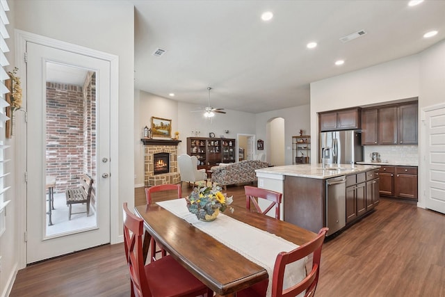 dining space with a stone fireplace, dark hardwood / wood-style floors, sink, and ceiling fan