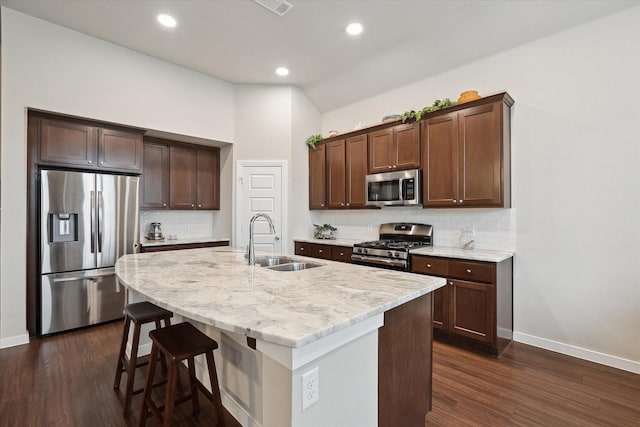 kitchen featuring sink, dark wood-type flooring, a center island with sink, stainless steel appliances, and a kitchen bar