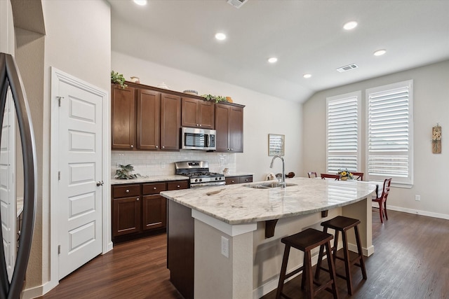 kitchen featuring appliances with stainless steel finishes, tasteful backsplash, an island with sink, sink, and light stone countertops