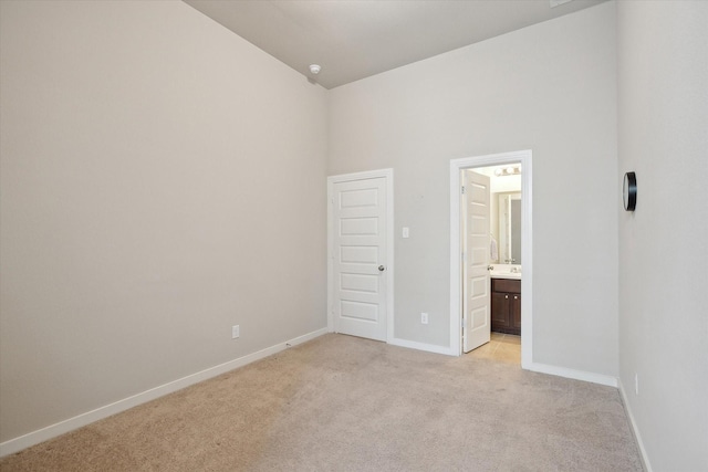 unfurnished bedroom with baseboards, light carpet, high vaulted ceiling, and connected bathroom