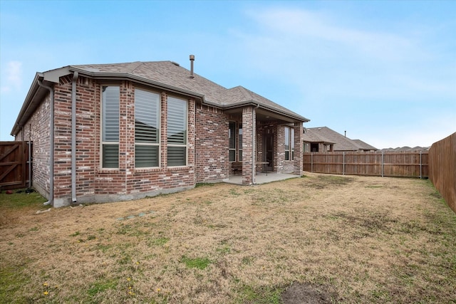 rear view of property with brick siding, a fenced backyard, a yard, and a patio