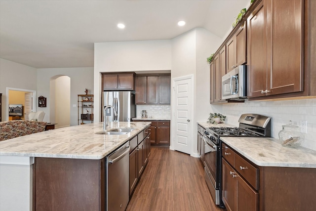 kitchen featuring a kitchen island with sink, appliances with stainless steel finishes, arched walkways, dark wood finished floors, and a sink