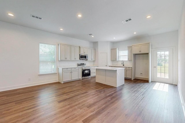 kitchen with sink, hardwood / wood-style flooring, a kitchen island, and appliances with stainless steel finishes