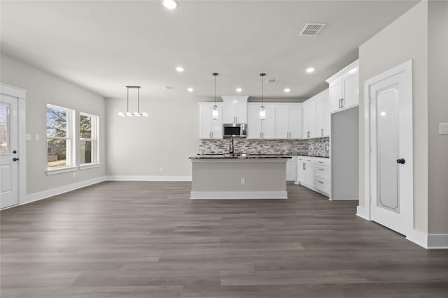 kitchen with white cabinetry, hanging light fixtures, backsplash, and an island with sink