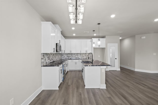 kitchen featuring sink, a kitchen island with sink, decorative backsplash, white cabinets, and decorative light fixtures