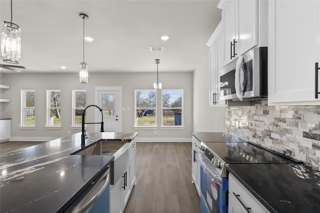 kitchen with tasteful backsplash, appliances with stainless steel finishes, hanging light fixtures, and white cabinets