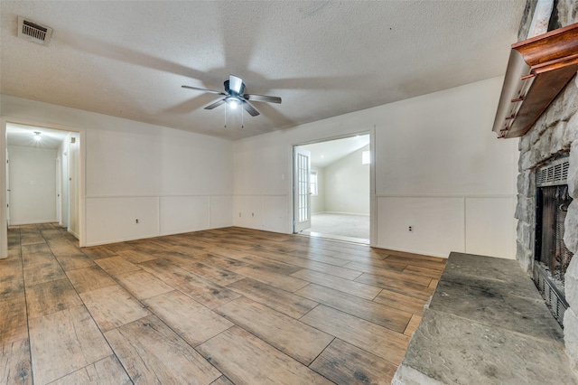 unfurnished living room with visible vents, ceiling fan, wood finished floors, a textured ceiling, and a fireplace