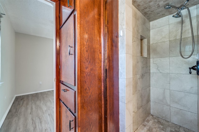 full bathroom featuring baseboards, a tile shower, and wood finished floors