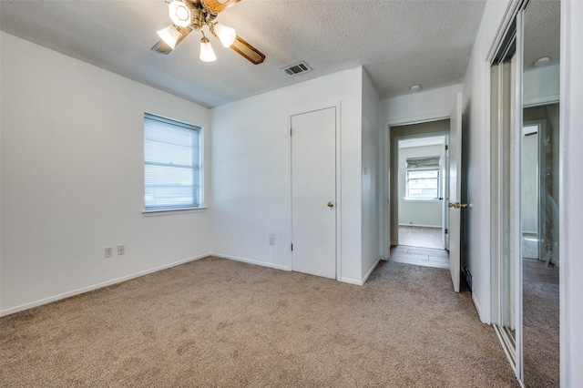 unfurnished bedroom with a textured ceiling, ceiling fan, light colored carpet, visible vents, and baseboards