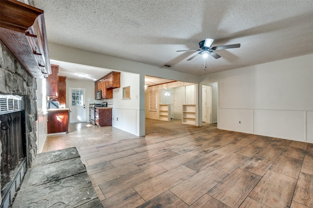 unfurnished living room featuring ceiling fan, a stone fireplace, wood finish floors, and a textured ceiling