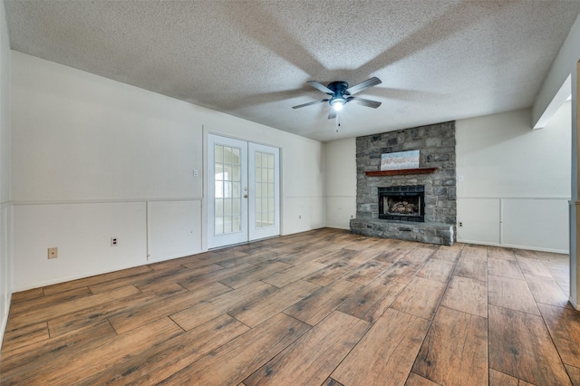 unfurnished living room with a stone fireplace, french doors, ceiling fan, and wood finished floors