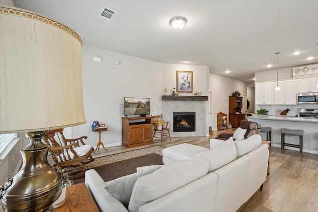 living area with visible vents, baseboards, light wood-style flooring, a fireplace, and recessed lighting