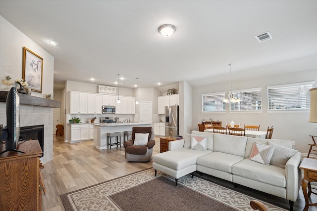 living room featuring a tiled fireplace, light hardwood / wood-style floors, and a notable chandelier