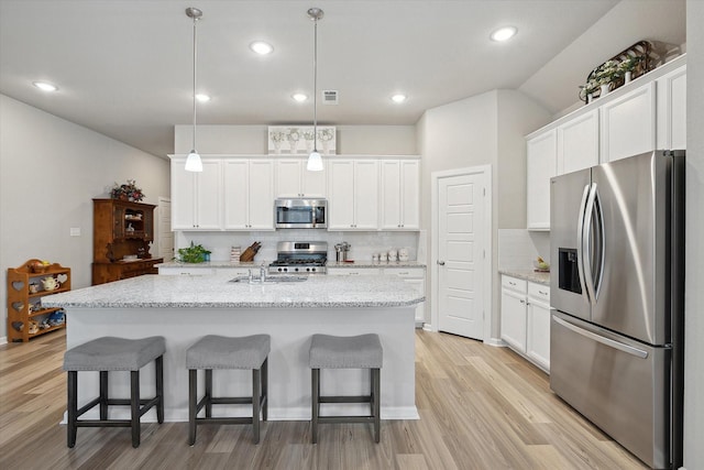 kitchen featuring appliances with stainless steel finishes, pendant lighting, white cabinets, a kitchen island with sink, and light stone countertops