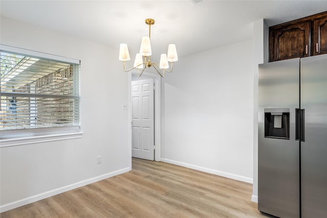 unfurnished dining area with a chandelier, light wood-style flooring, and baseboards