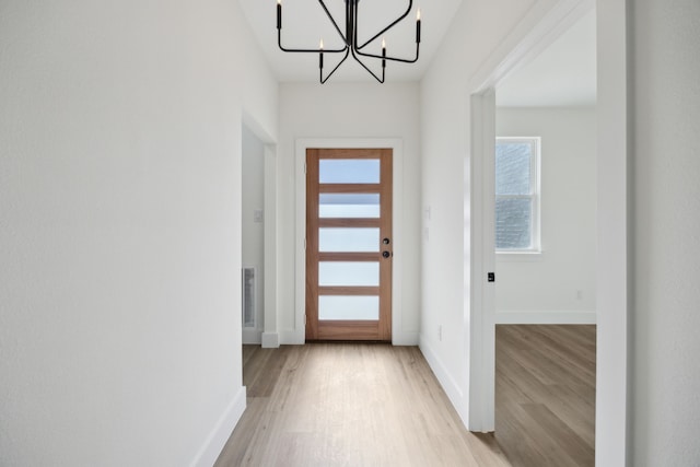 doorway to outside with an inviting chandelier and light hardwood / wood-style flooring