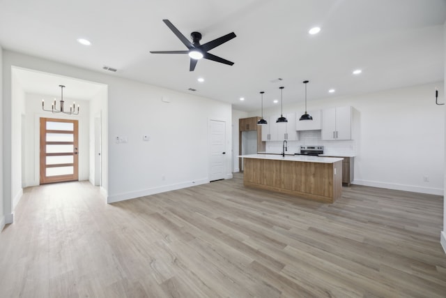 kitchen featuring stainless steel range with electric stovetop, hanging light fixtures, a large island with sink, light wood-type flooring, and white cabinets