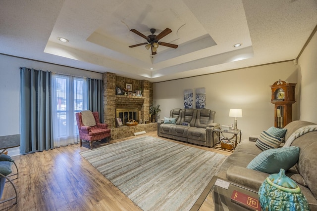 living room featuring crown molding, light hardwood / wood-style flooring, a tray ceiling, ceiling fan, and a fireplace