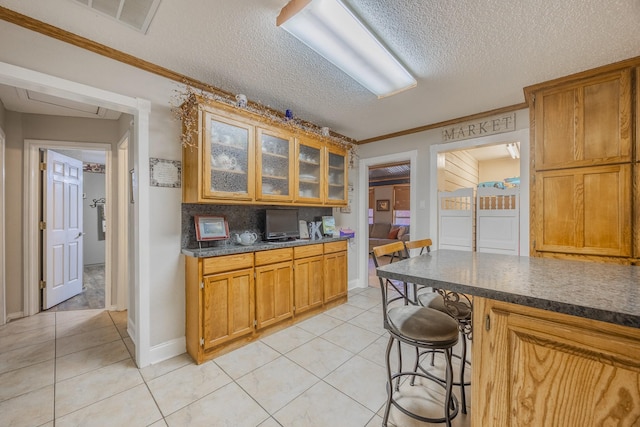 kitchen with a breakfast bar area, decorative backsplash, ornamental molding, light tile patterned floors, and a textured ceiling