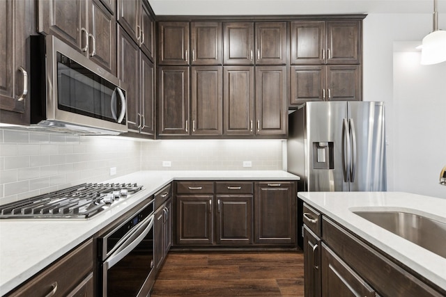 kitchen with dark wood-type flooring, sink, pendant lighting, stainless steel appliances, and backsplash