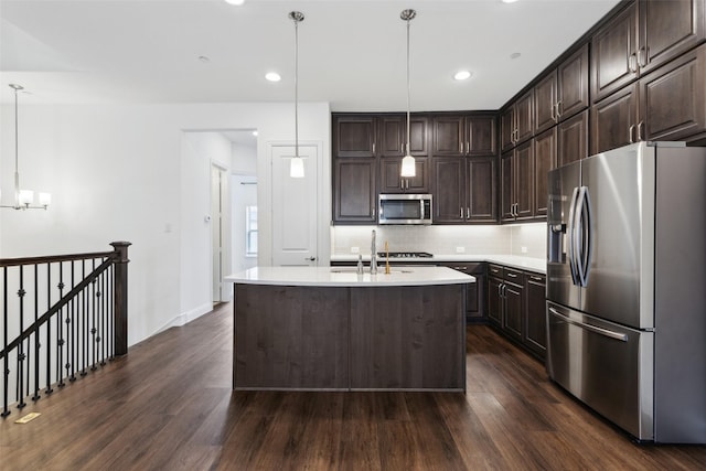 kitchen with hanging light fixtures, stainless steel appliances, dark brown cabinetry, tasteful backsplash, and an island with sink