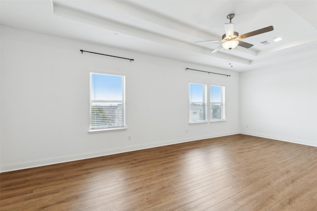 empty room featuring hardwood / wood-style flooring, ceiling fan, and a raised ceiling