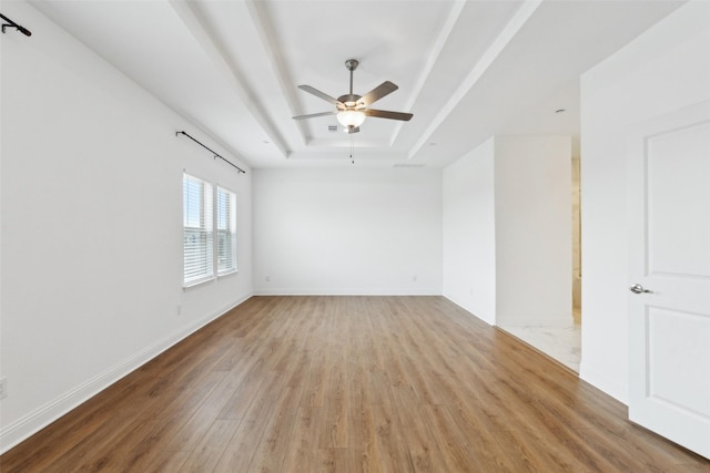 empty room with ceiling fan, a tray ceiling, and light hardwood / wood-style floors