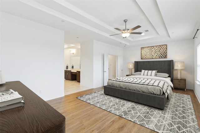 bedroom with ensuite bath, light hardwood / wood-style floors, a raised ceiling, and ceiling fan