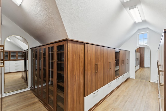 hall with vaulted ceiling, a textured ceiling, and light wood-type flooring