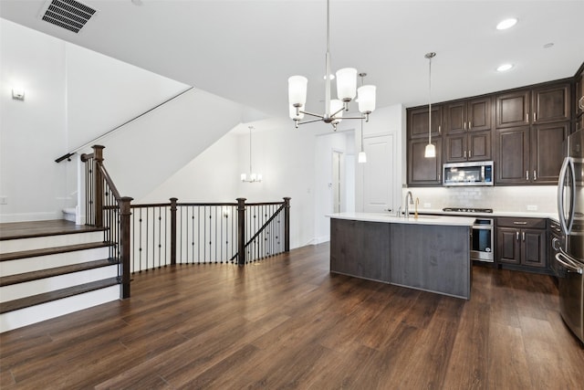 kitchen with appliances with stainless steel finishes, decorative light fixtures, dark hardwood / wood-style flooring, a chandelier, and a center island with sink