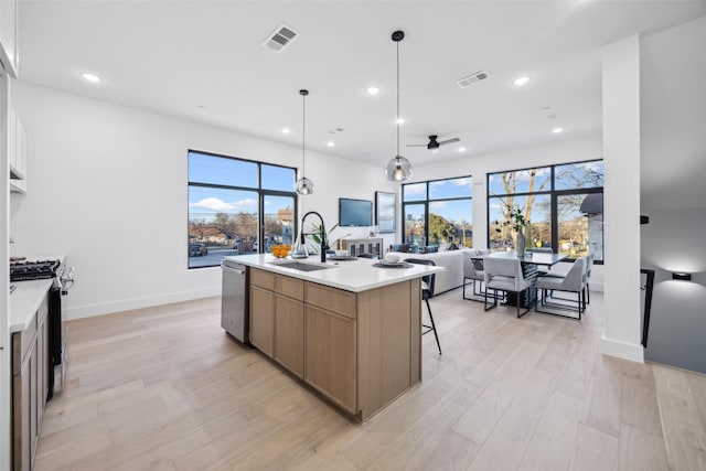 kitchen featuring sink, hanging light fixtures, stainless steel appliances, an island with sink, and white cabinets