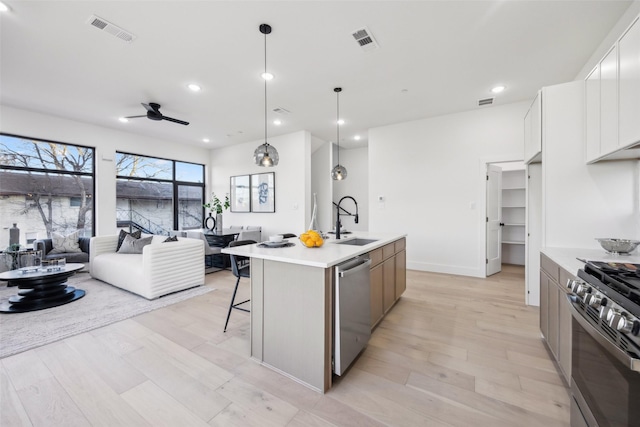 kitchen with sink, white cabinetry, appliances with stainless steel finishes, pendant lighting, and a kitchen island with sink