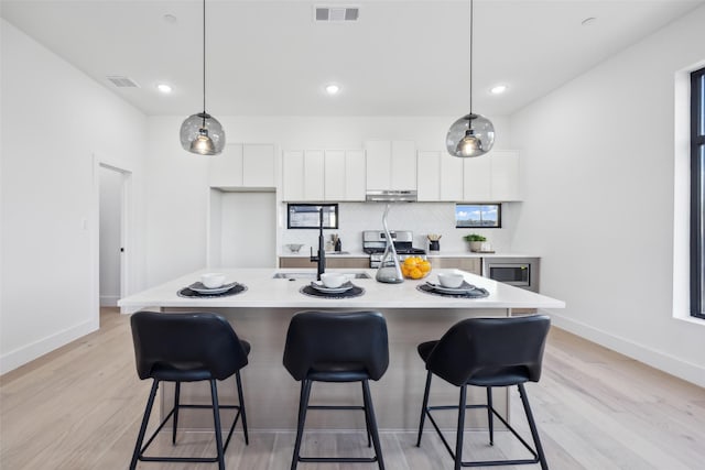 kitchen with a kitchen island with sink, pendant lighting, tasteful backsplash, and white cabinets