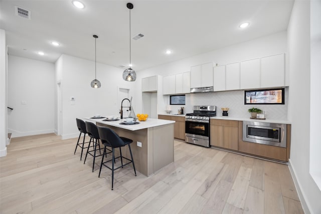 kitchen featuring tasteful backsplash, decorative light fixtures, stainless steel appliances, a kitchen island with sink, and white cabinets