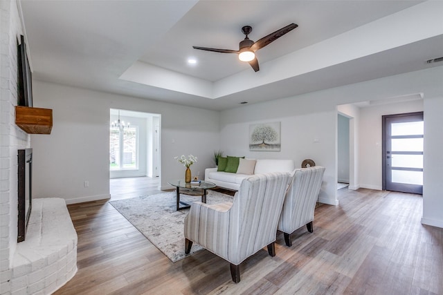 living room with a raised ceiling, ceiling fan with notable chandelier, hardwood / wood-style floors, and a fireplace