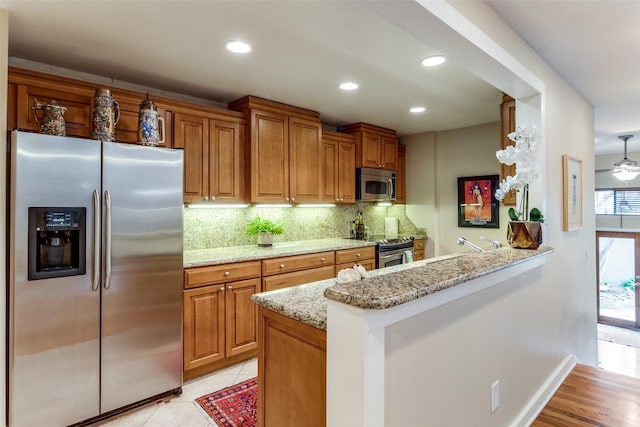 kitchen with light tile patterned floors, backsplash, stainless steel appliances, light stone countertops, and kitchen peninsula