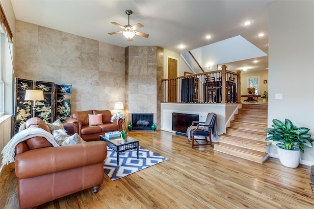 living room featuring lofted ceiling, light hardwood / wood-style flooring, tile walls, a tile fireplace, and ceiling fan