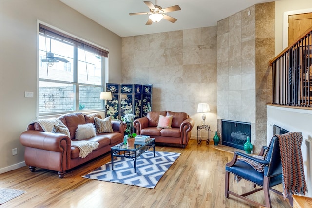 living room with a tiled fireplace, hardwood / wood-style floors, tile walls, and ceiling fan